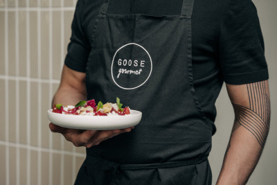 Eine Person mit einem angerichteten Teller in der Hand mit einer Schürze von GOOSE Gourmet Catering Frankfurt.